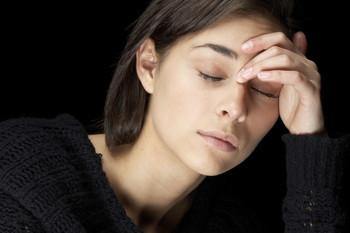 Woman with eyes closed holding forehead, appearing fatigued or unwell, on dark background
