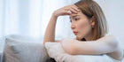 Thoughtful woman sitting on couch, resting head on arm, looking pensive indoors